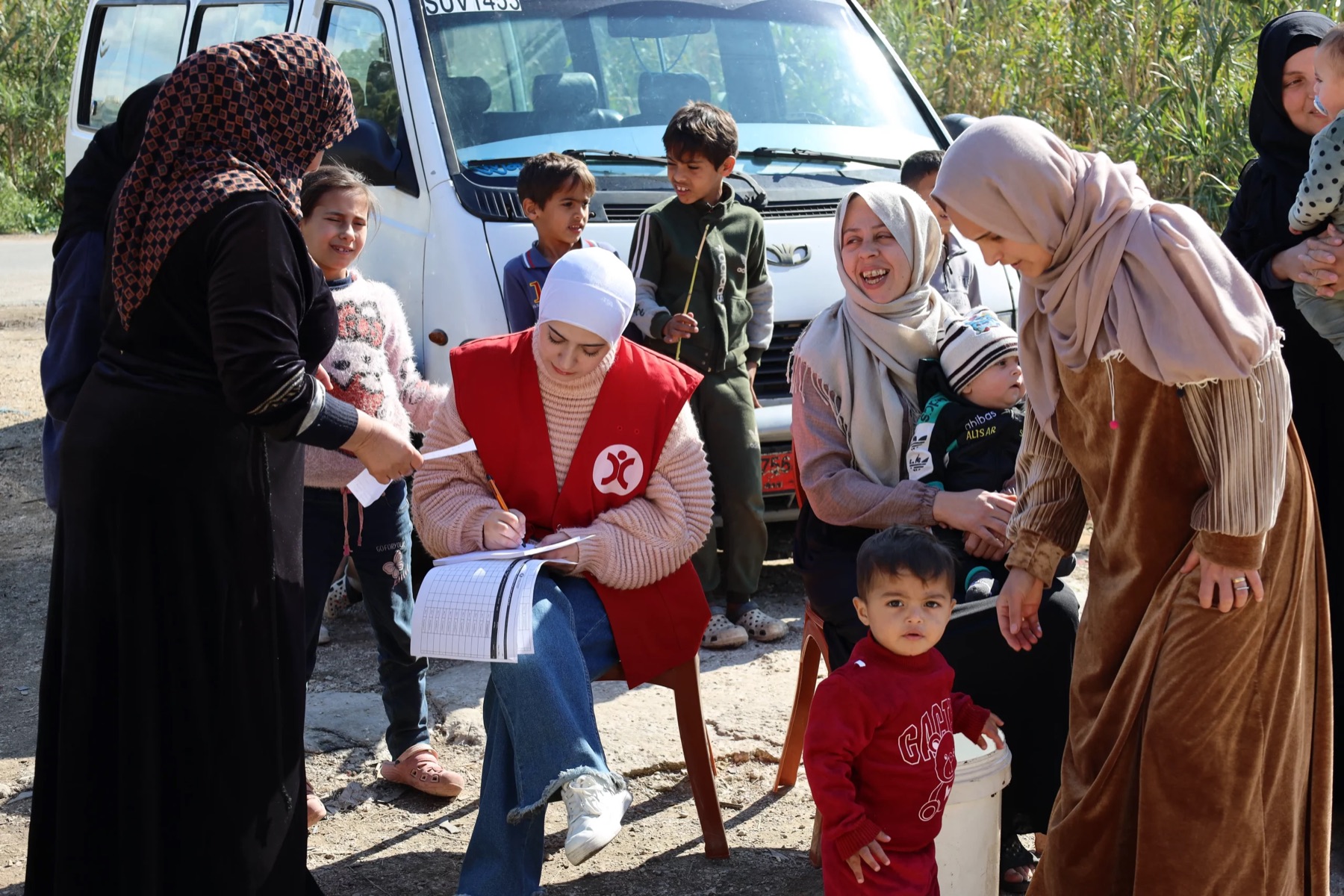 HCI field staff distributing aid to a queue of women and children beside a delivery van.