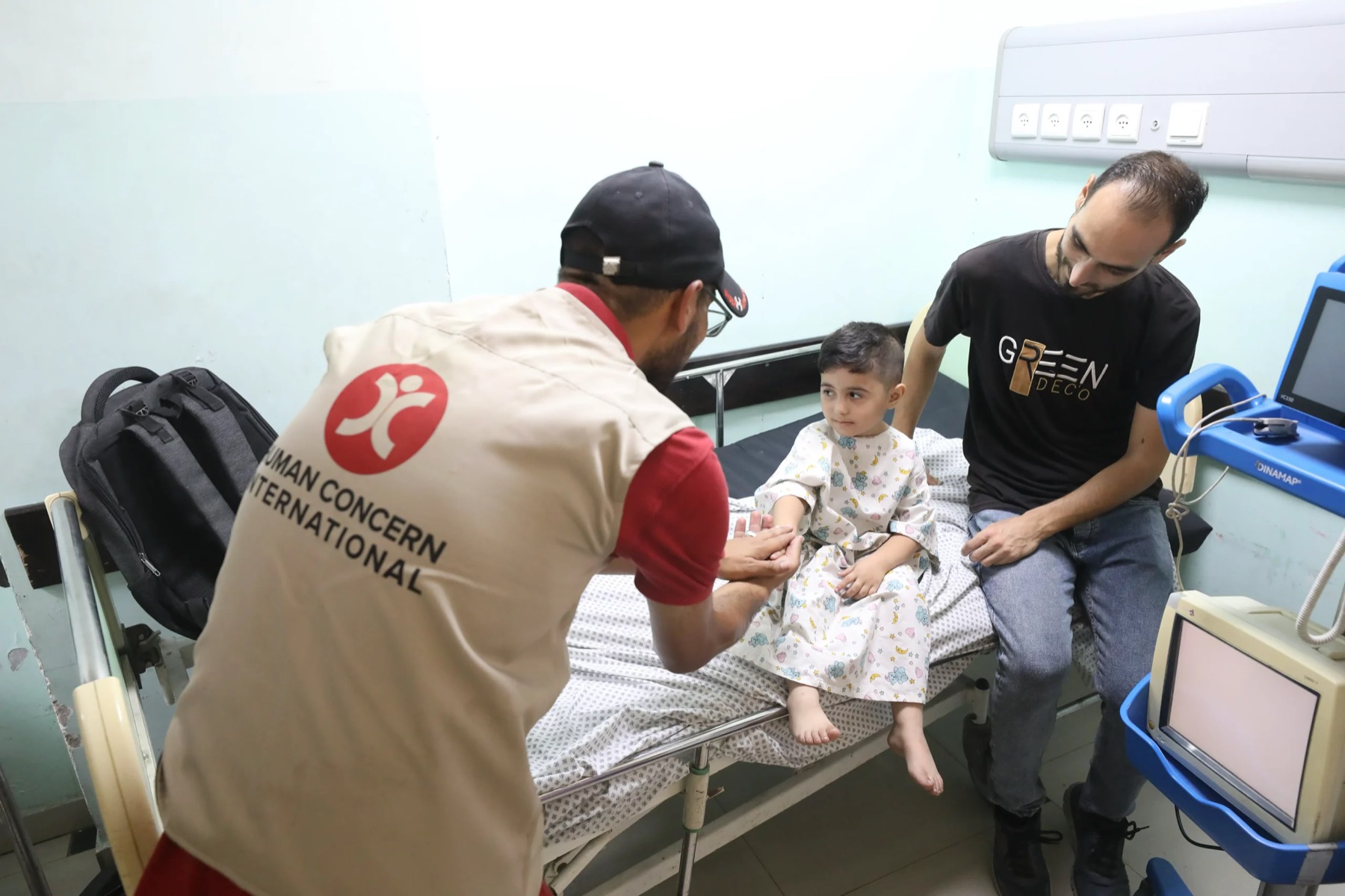 An HCI aid worker and a doctor treating a young child on a hospital bed.