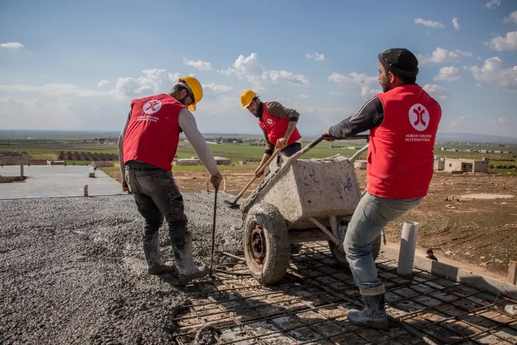 Three HCI workers in red vests laying a concrete foundation on a rural build site.